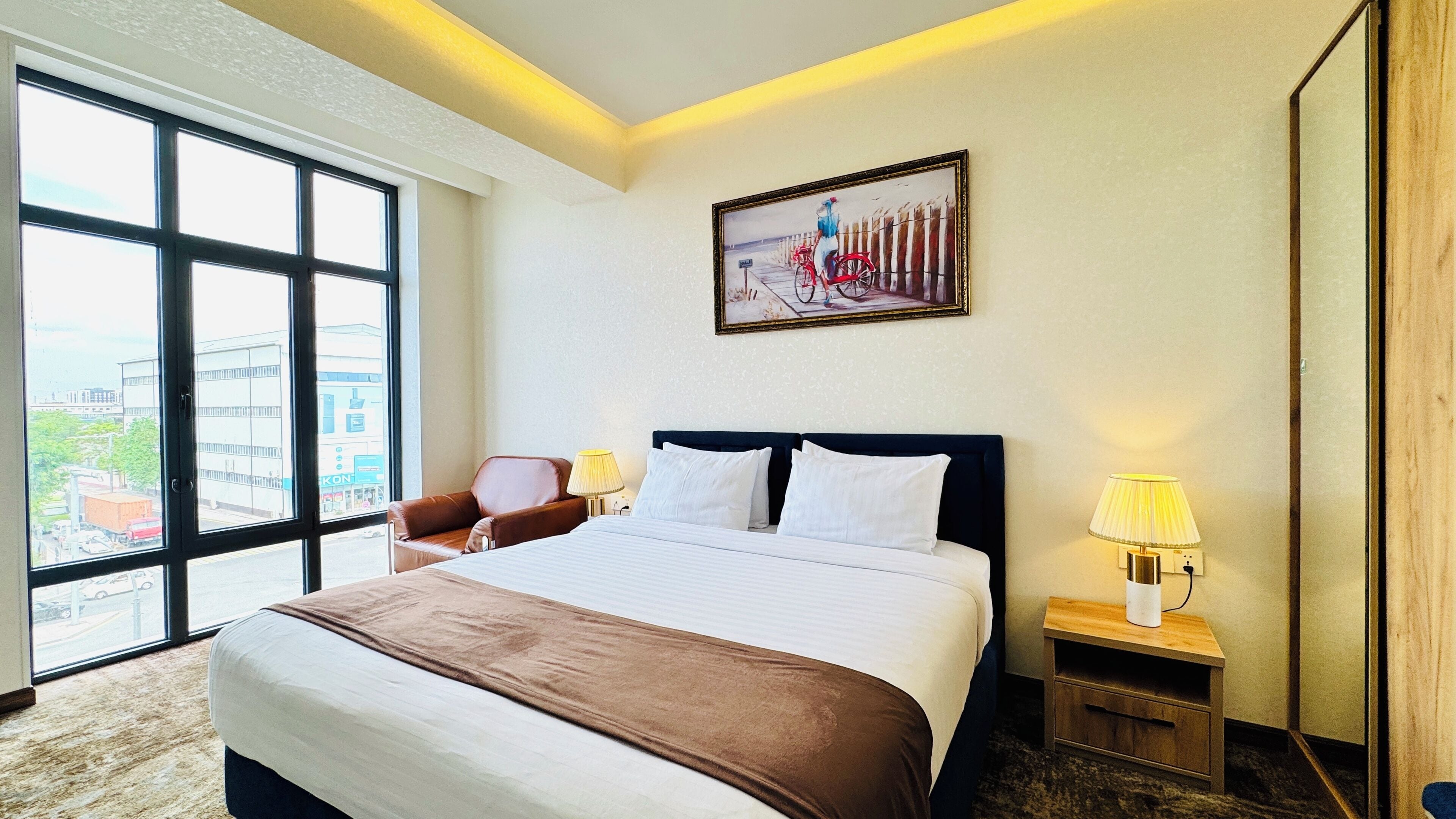 Un cuarto de hotel con una cama grande, una silla, una mesita de noche, una lámpara y un cuadro en la pared.