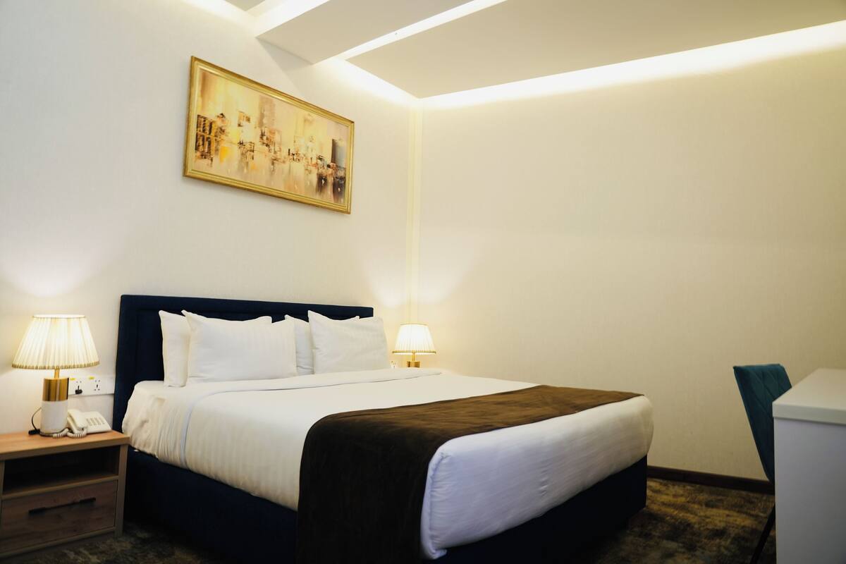 Une chambre d’hôtel avec un lit bien fait, des lampes de chevet, un tableau au mur et un bureau avec une chaise.