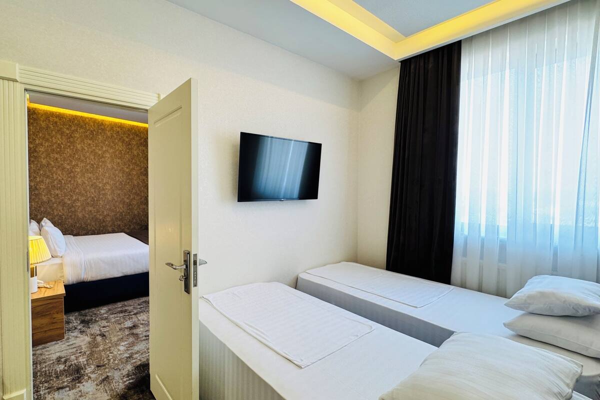 Une chambre d’hôtel avec un lit, une table de chevet, un téléviseur fixé au mur et une fenêtre avec des rideaux.