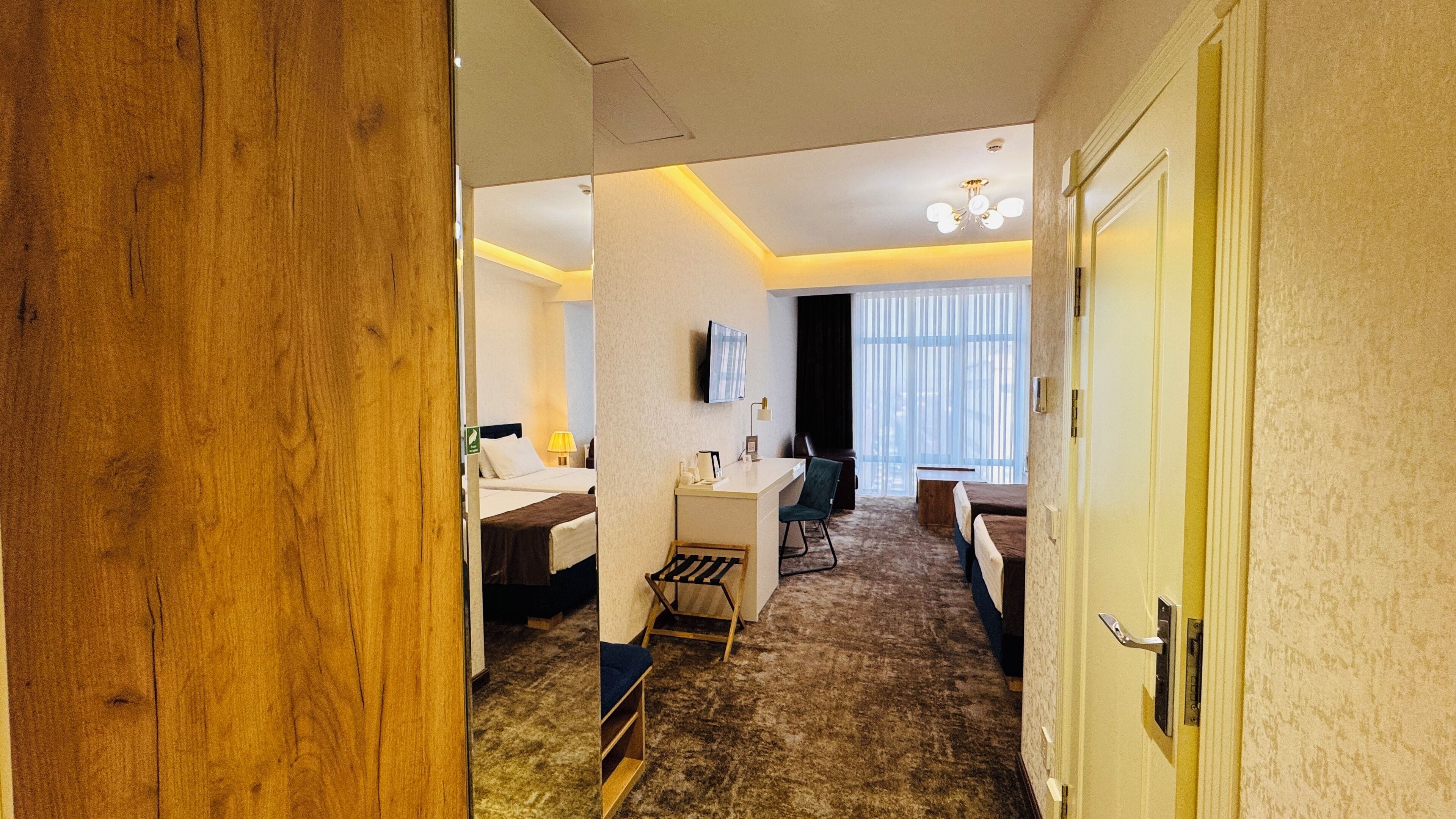 A hotel room with a bed, bedside table, lamp, and a small desk with a chair.