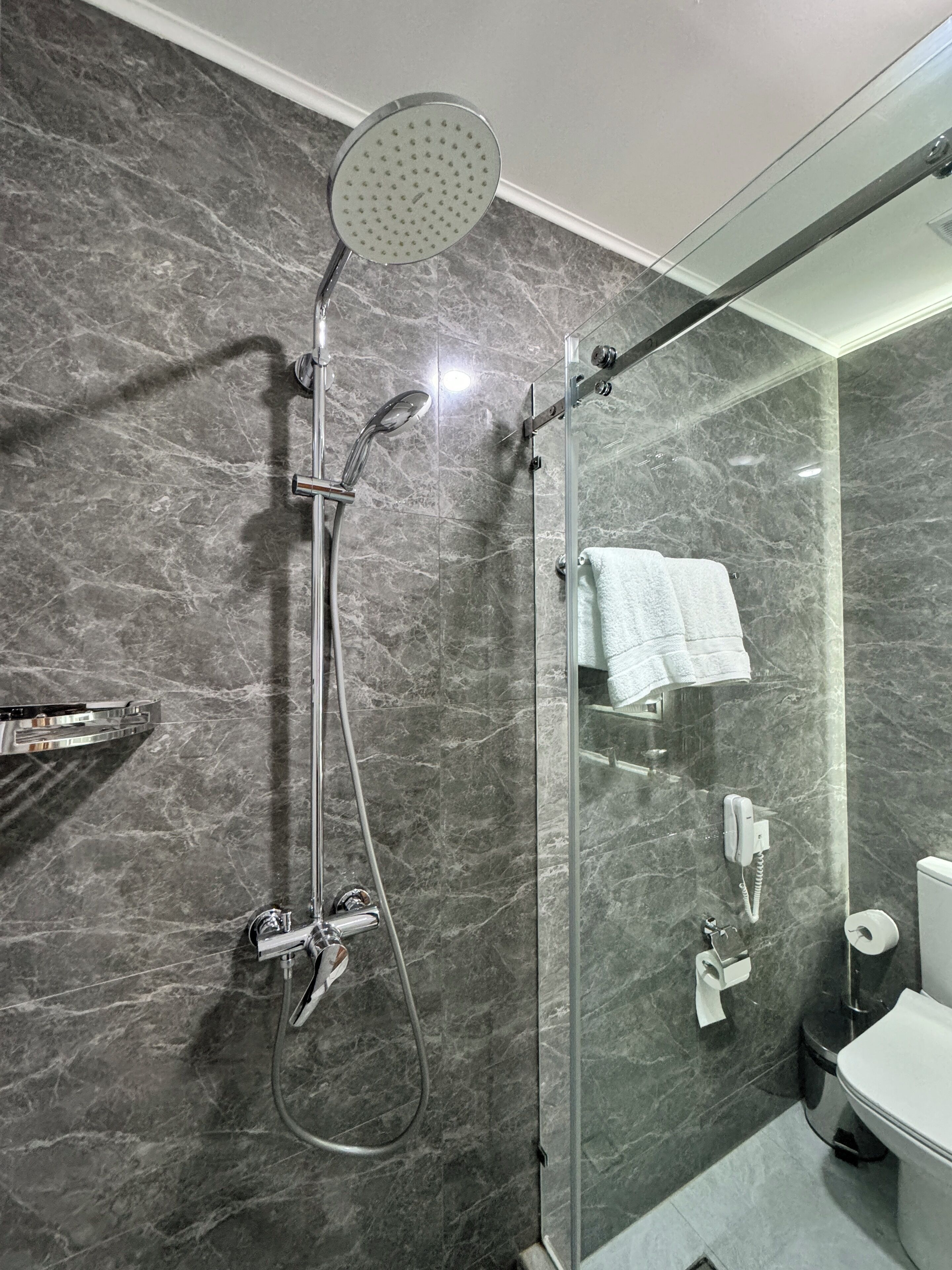 Ein modernes Badezimmer mit einer Duschkabine, Marmorwänden, einer weißen Toilette und einer Glasduschtür.