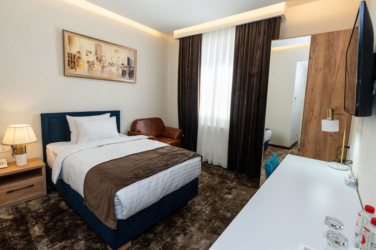 Une chambre d’hôtel avec un lit, un bureau, une chaise, un tableau et un téléviseur.