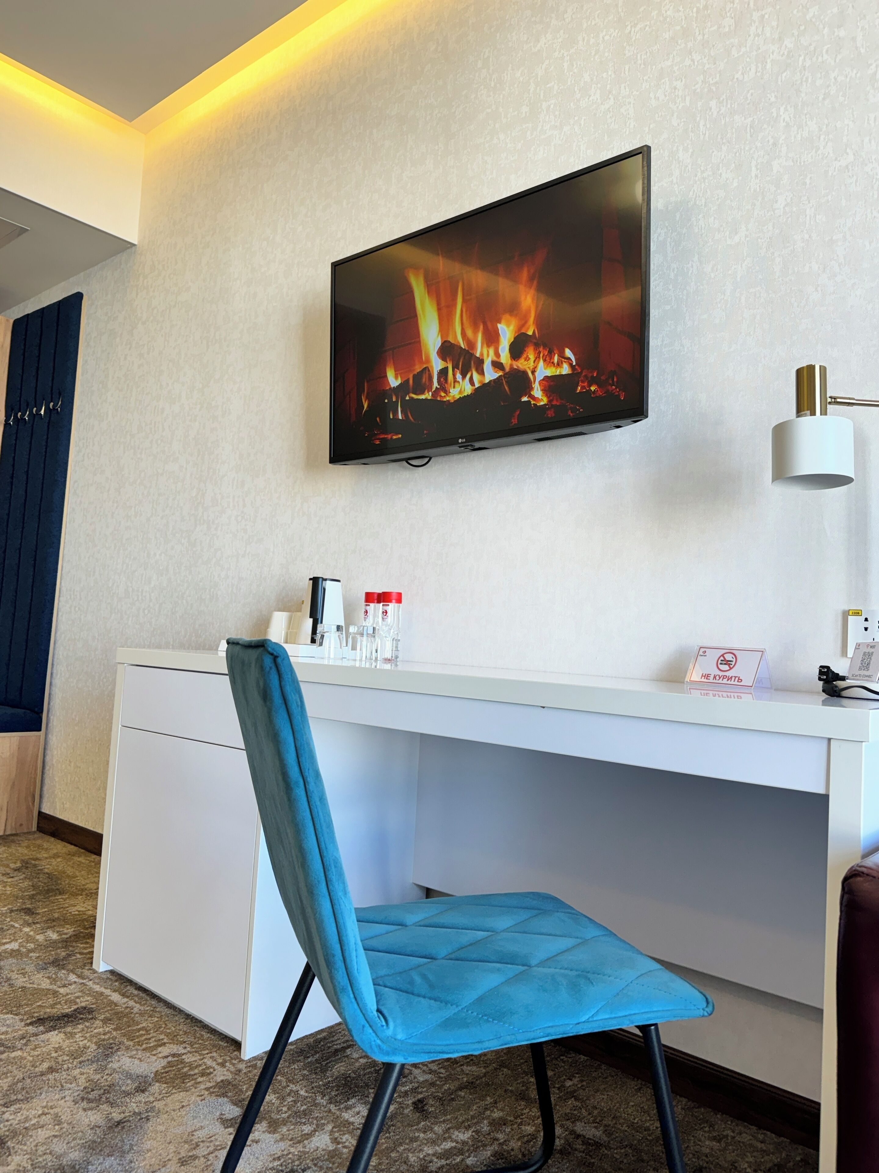 Une chambre d’hôtel équipée d’un téléviseur à écran plat fixé au mur, sur lequel est affichée une image de cheminée, d’un bureau avec une chaise et d’un panneau indiquant « Il est interdit de fumer ».