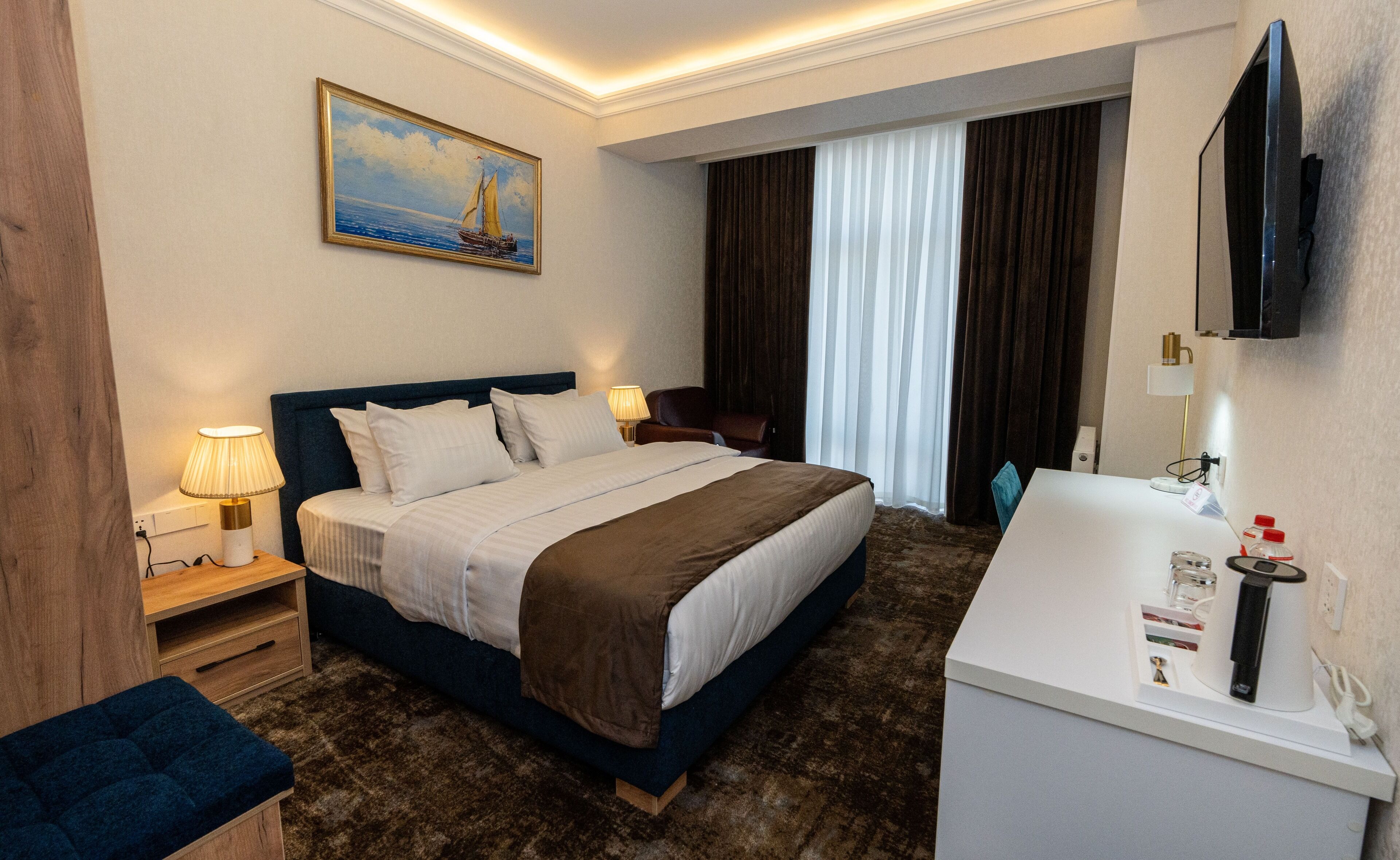 Une chambre d’hôtel avec un lit, des lampes de chevet, un tableau, une télévision et une salle de bain équipée d’un lavabo et d’un miroir.