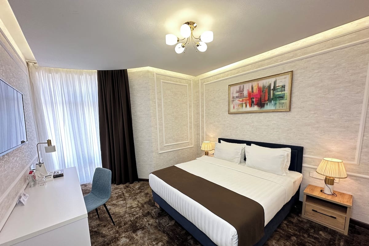Une chambre d’hôtel avec un lit, un bureau, une chaise et un tableau au mur.