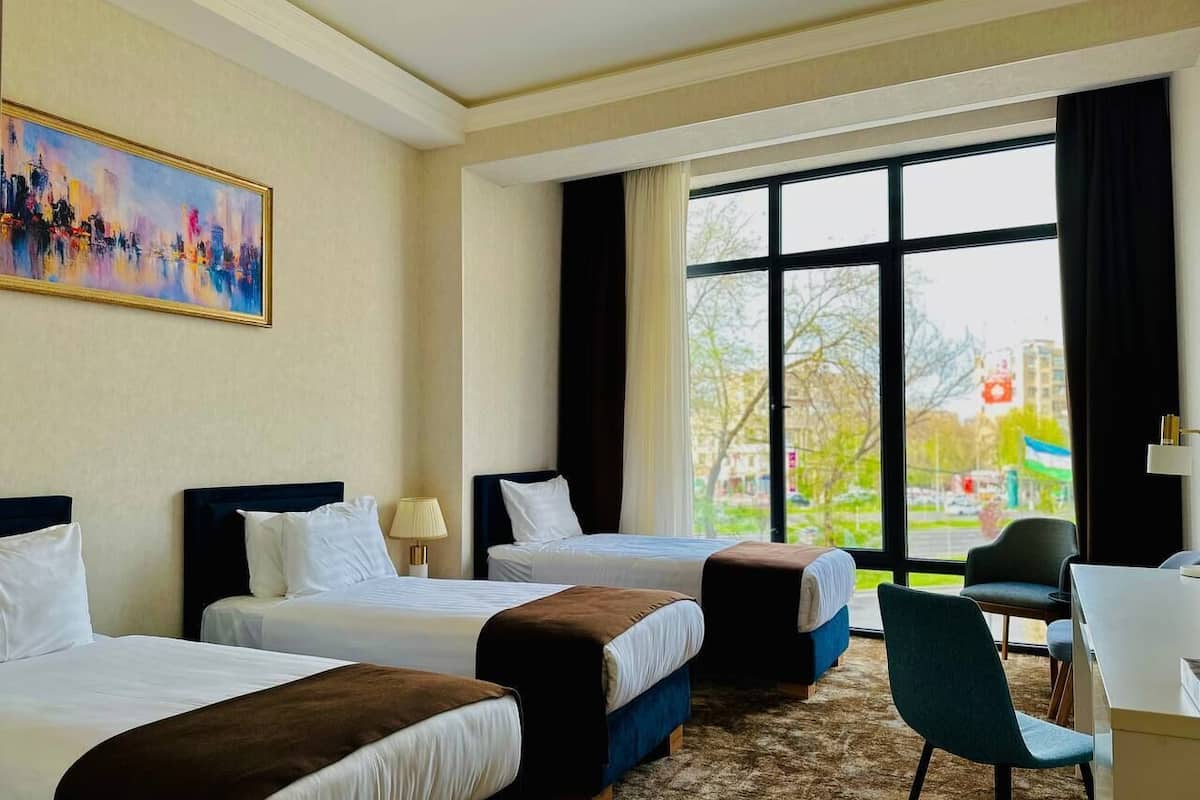 Une chambre d’hôtel avec deux lits, un bureau et une chaise. Il y a une grande fenêtre donnant sur l’extérieur.