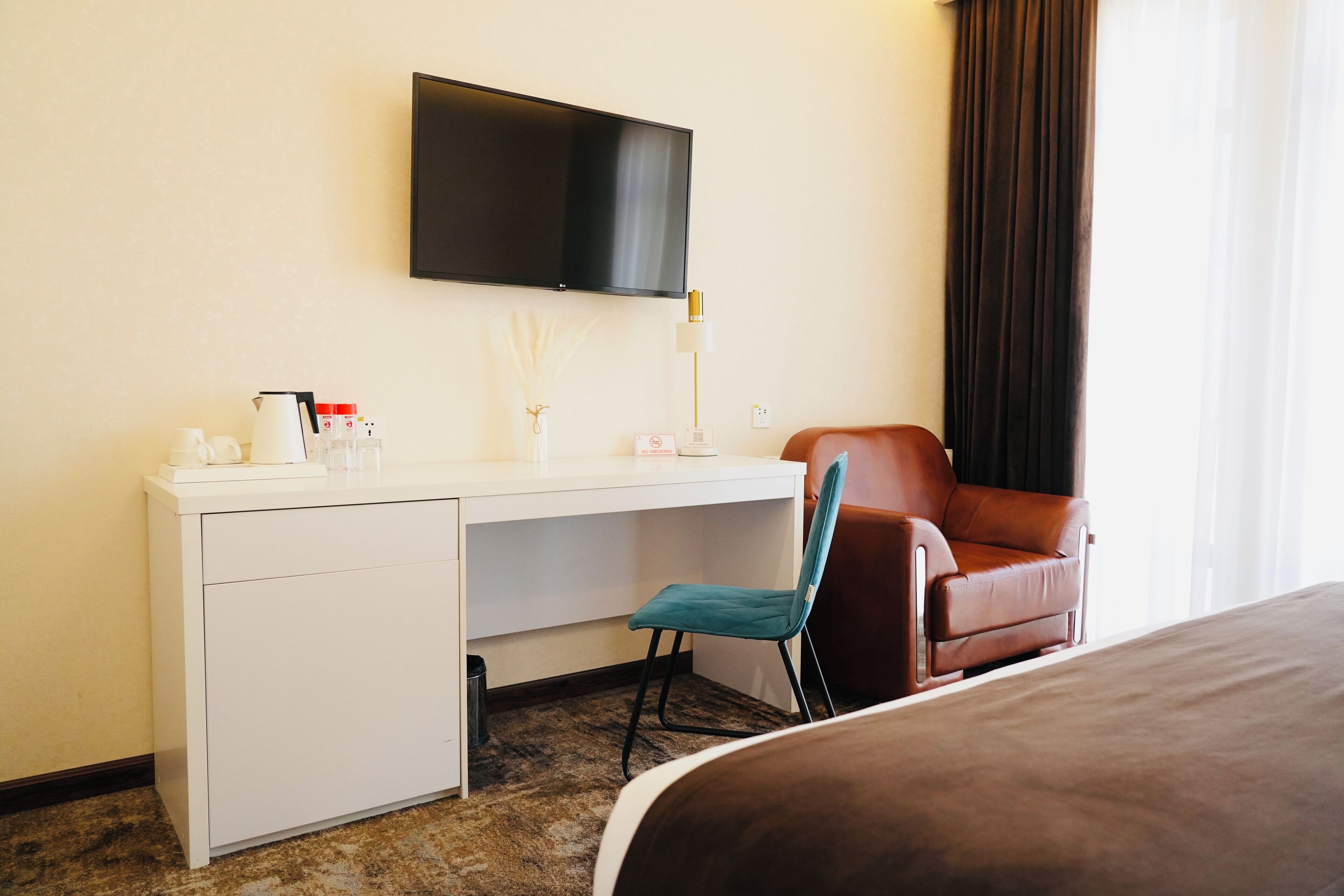 Una habitación de hotel con cama, escritorio, silla, televisión y ventana con cortinas.