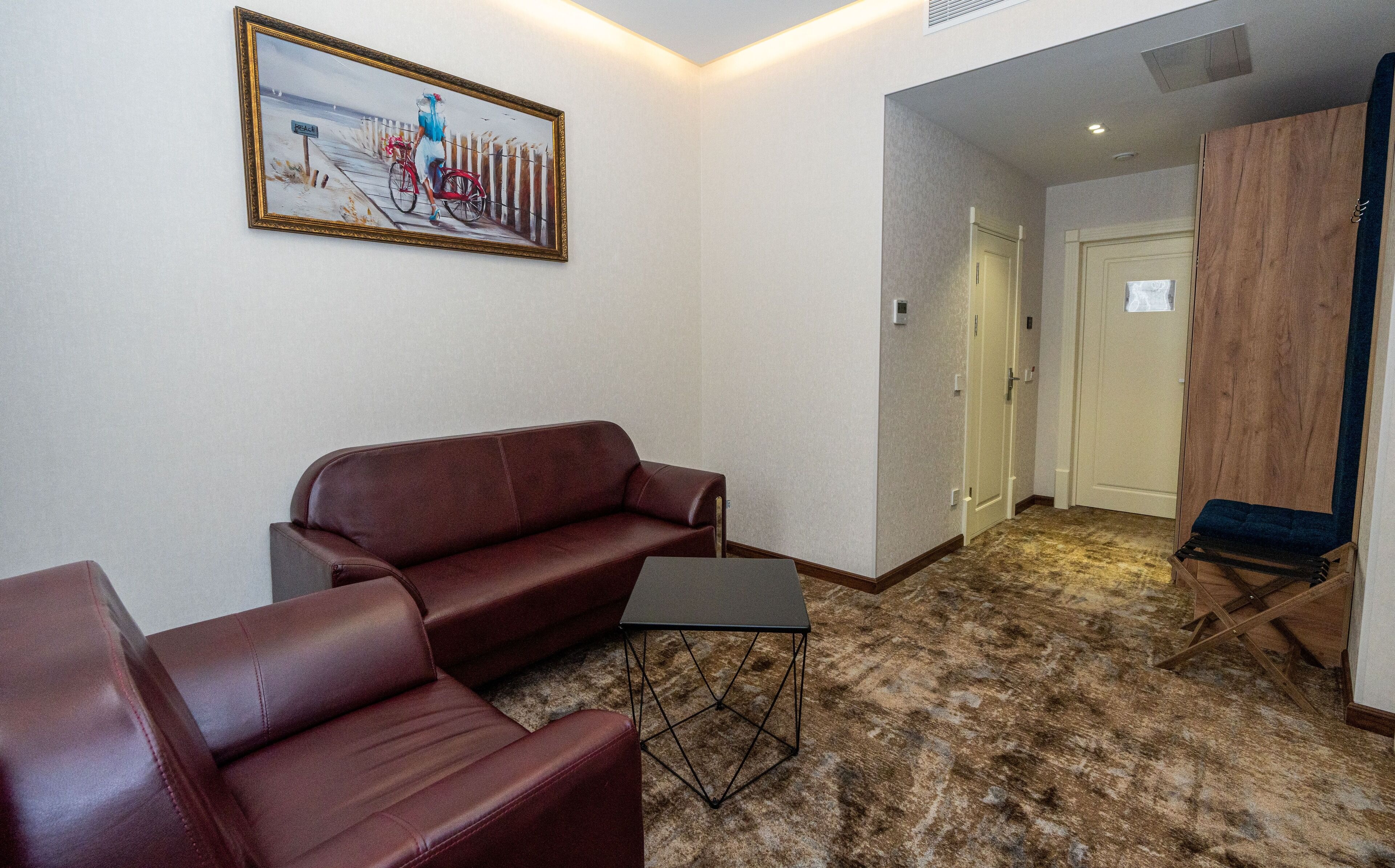 Una habitación con un sofá de cuero marrón, una mesita negra y un cuadro de una playa en la pared.