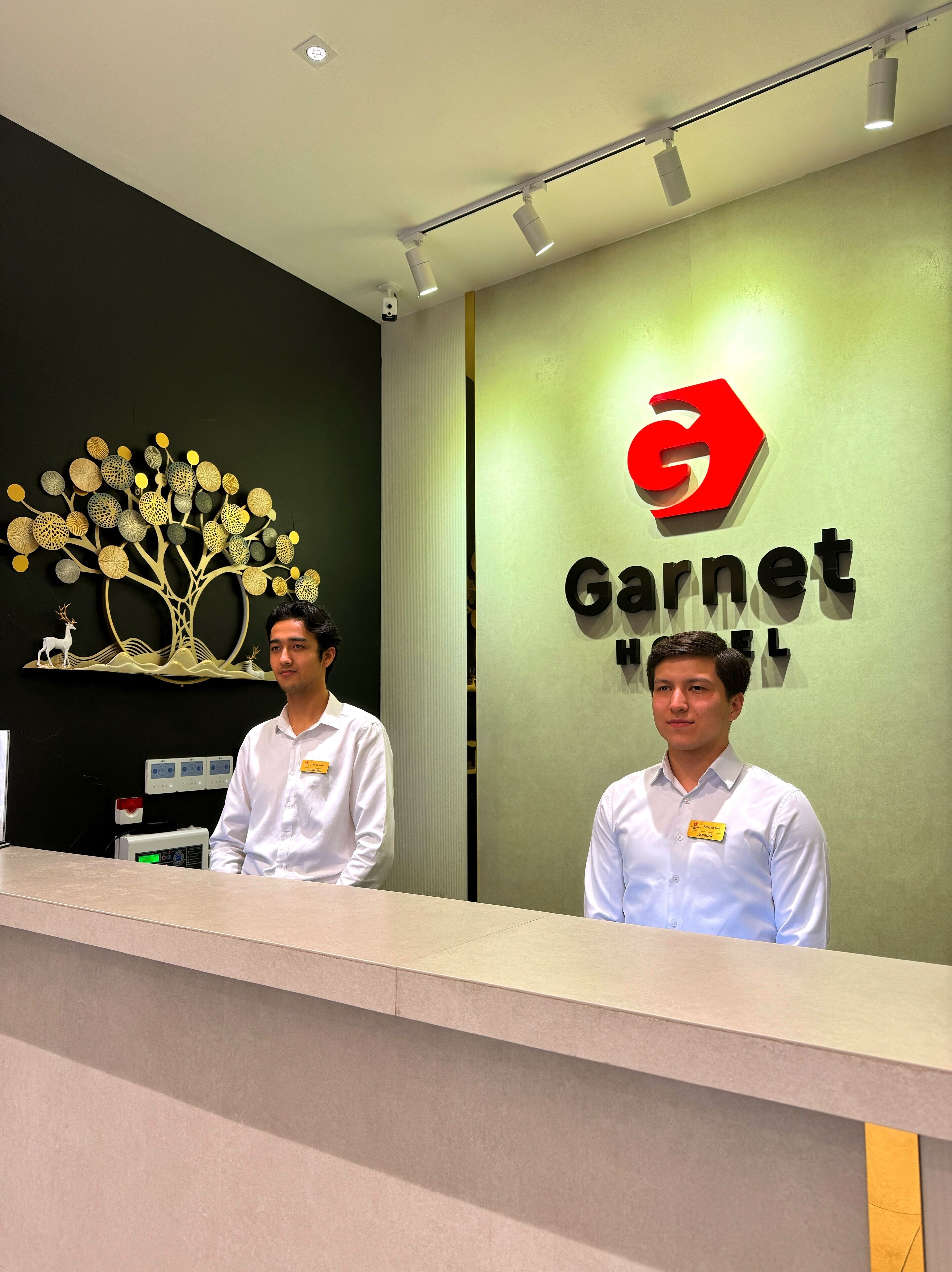 A reception desk with a Garnet Hotel sign, a decorative tree mural, and a name tag holder.