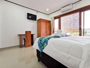A hotel room with a bed, a wooden wardrobe, a small wooden table, a flat-screen TV mounted on the wall, and an air conditioning unit.