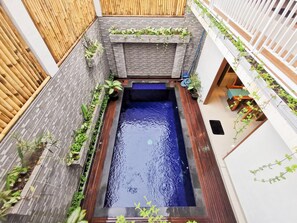 Une piscine rectangulaire avec un élément décoratif aquatique d’un bleu foncé, entourée d’une terrasse en bois et d’un mur de briques agrémenté de verdure.