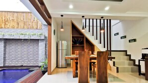 A modern kitchen with a built-in refrigerator, wooden dining table, and chairs. There is a staircase with black railings leading to an upper level. - Sunny Apartico Villa (Ungasan)