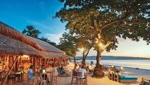A beachside restaurant with outdoor seating, a thatched-roof structure, and a view of the sea. - Sunny Apartico Villa (Ungasan)