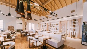 A spacious restaurant with wooden floors, white furniture, and pendant lighting.