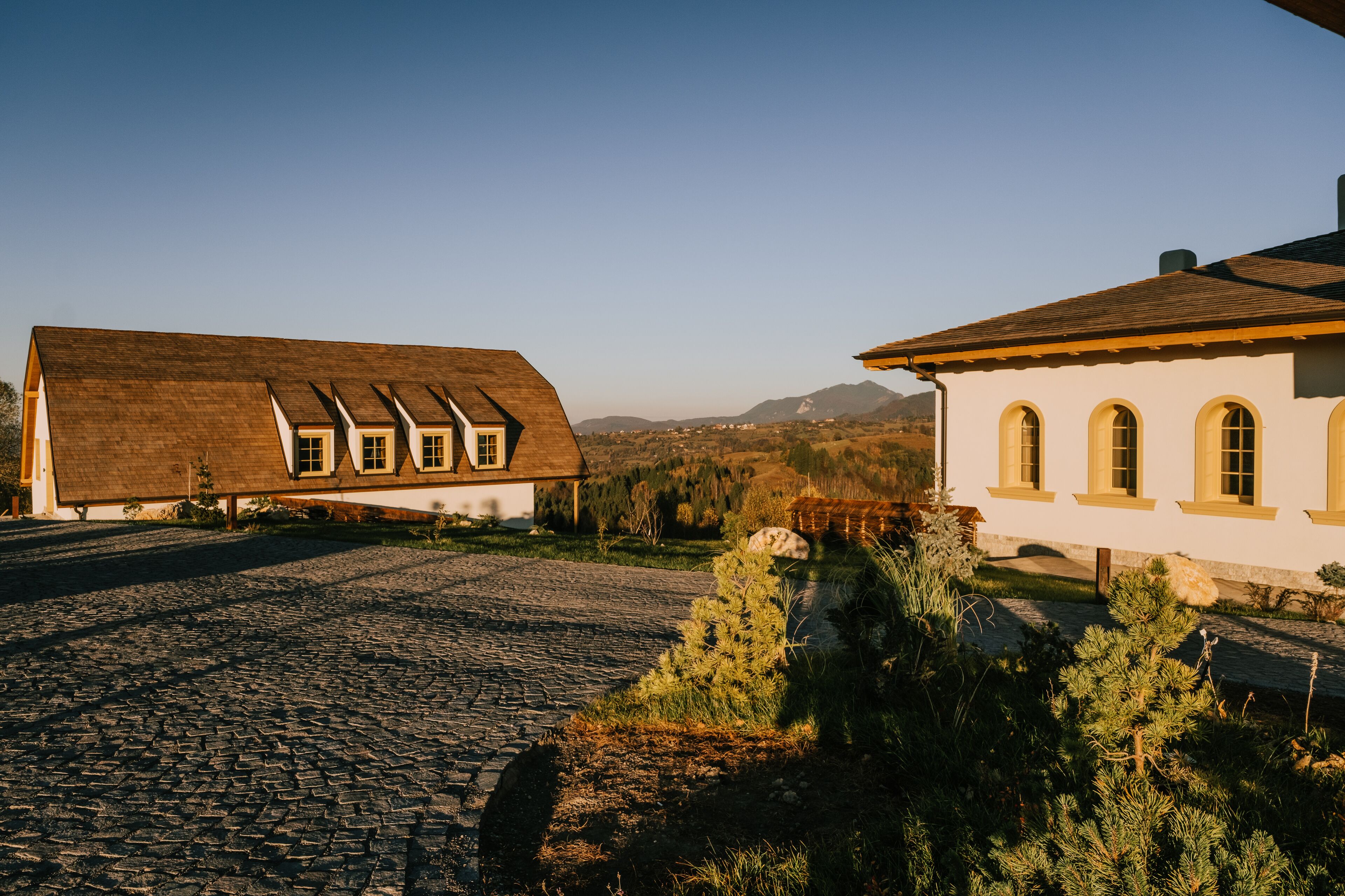 A rustic building with a cobblestone driveway and a mountain backdrop.
