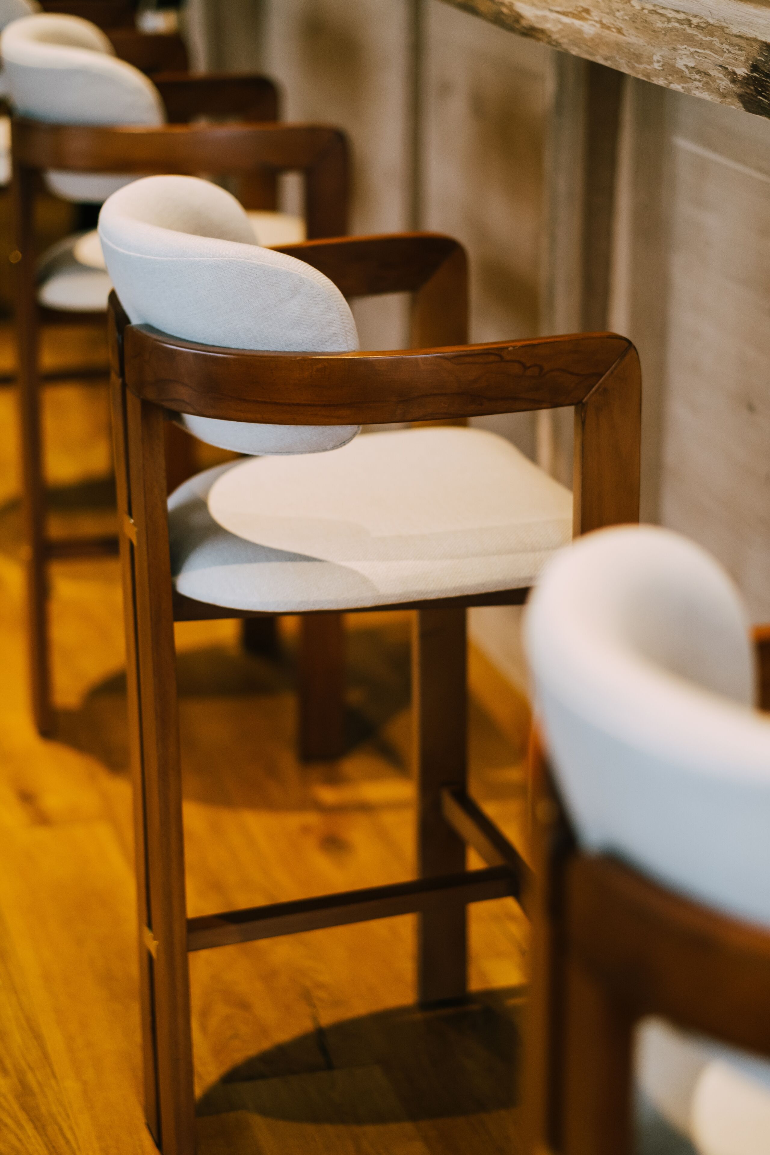 A row of wooden chairs with white cushions in a restaurant setting.