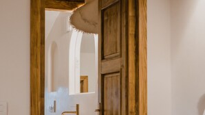 A bedroom with a wooden door, a bed, and a small wooden table with toiletries.