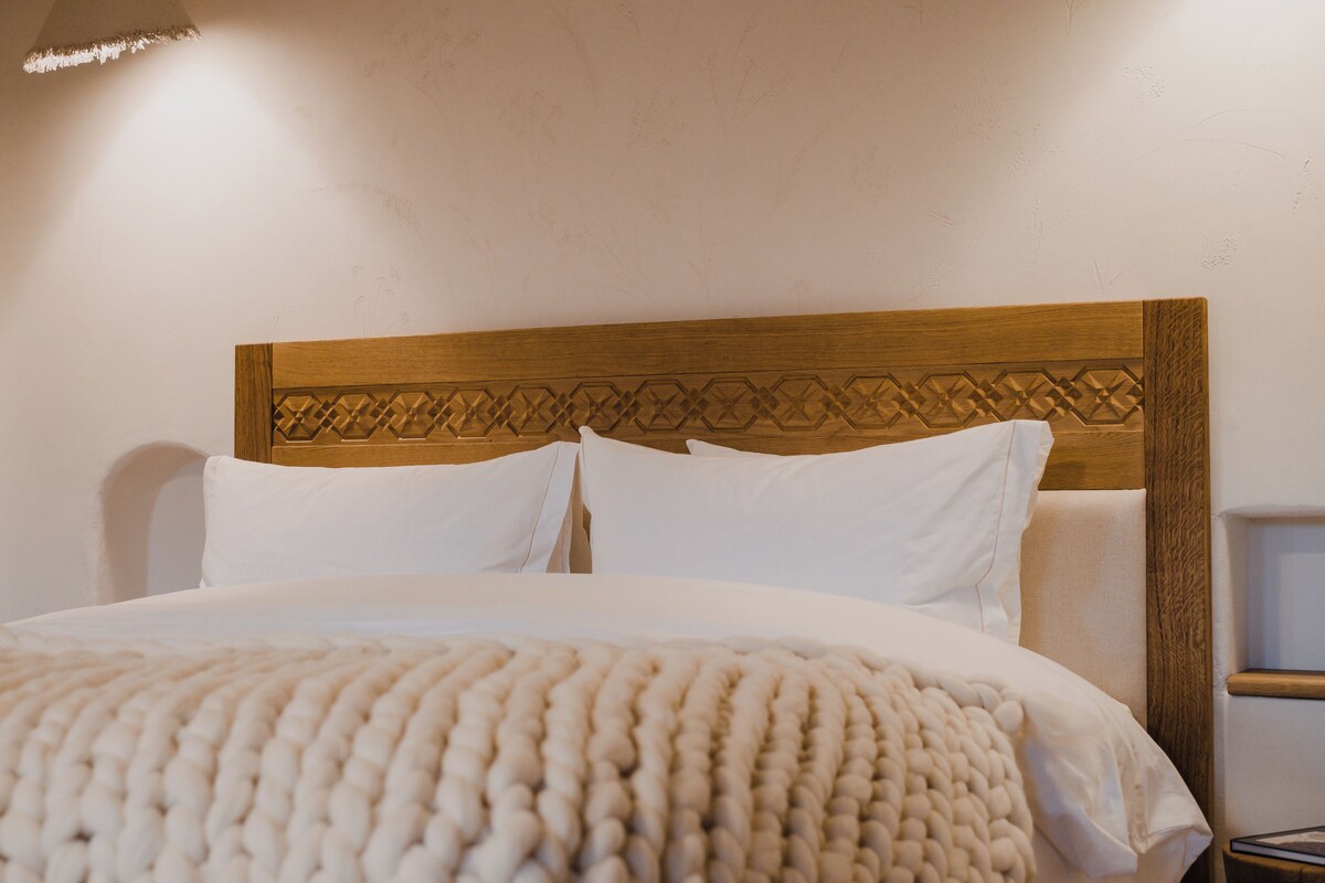 A neatly made bed with a wooden headboard, white bedding, and a textured throw blanket.