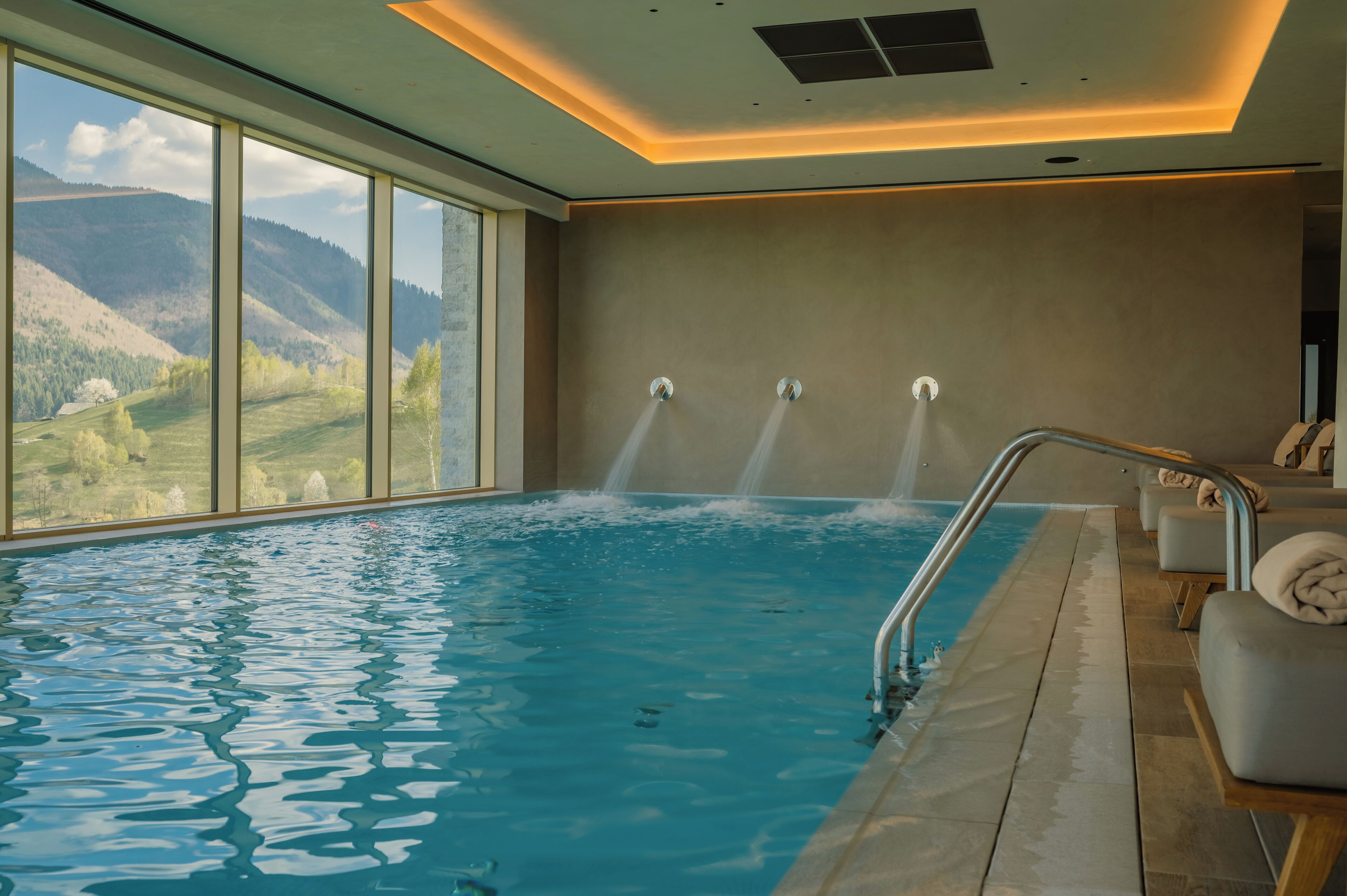 An indoor swimming pool with a view of mountains, a sauna area, and a modern ceiling design.