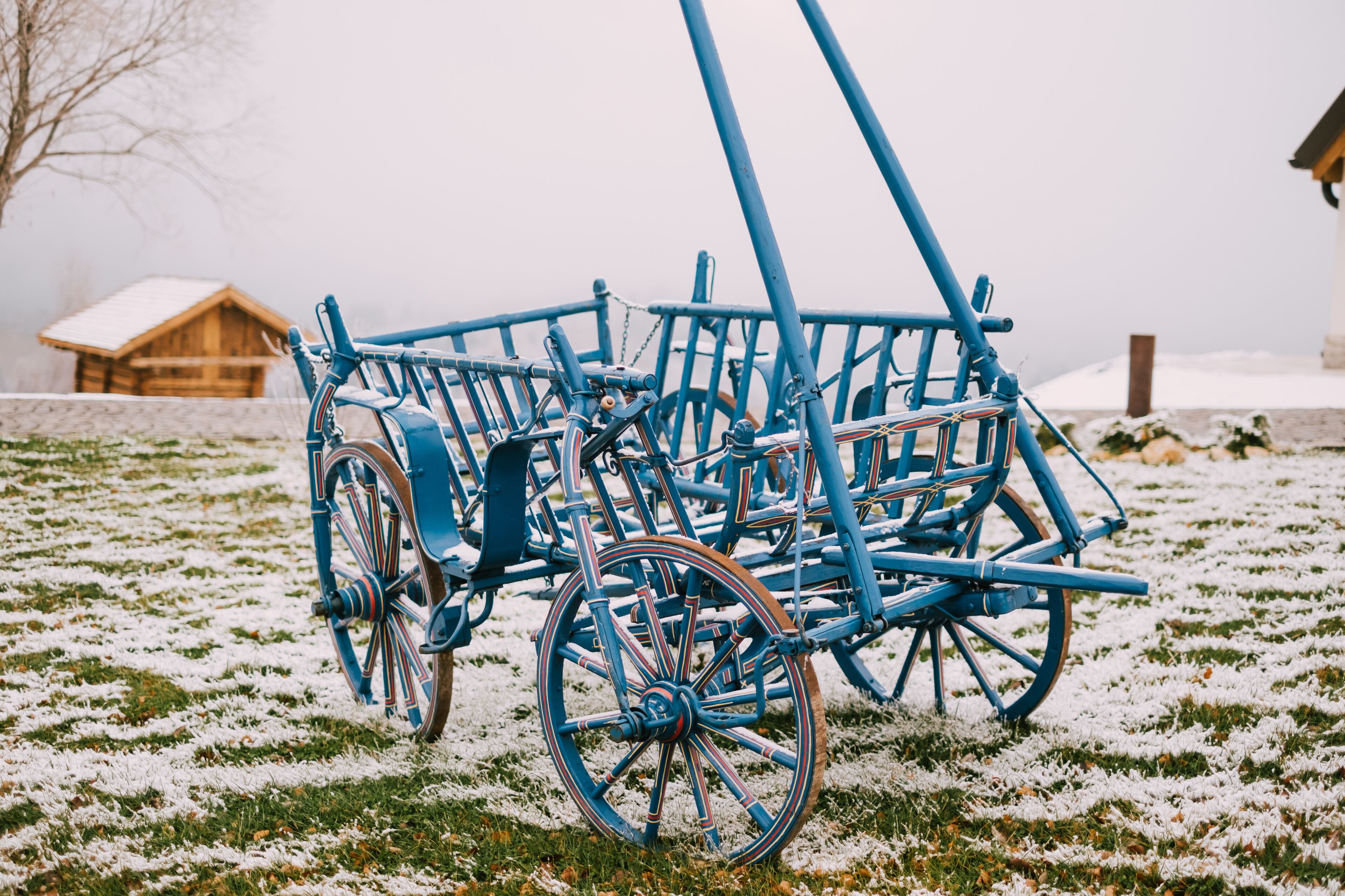 A blue wooden structure with wheels, possibly a cart or equipment, on a grassy field with snow patches.