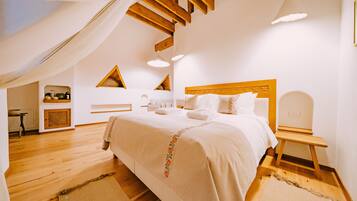 Ein Schlafzimmer mit einem großen Bett, Holzbalken, einem Oberlicht und einem kleinen Schreibtisch.