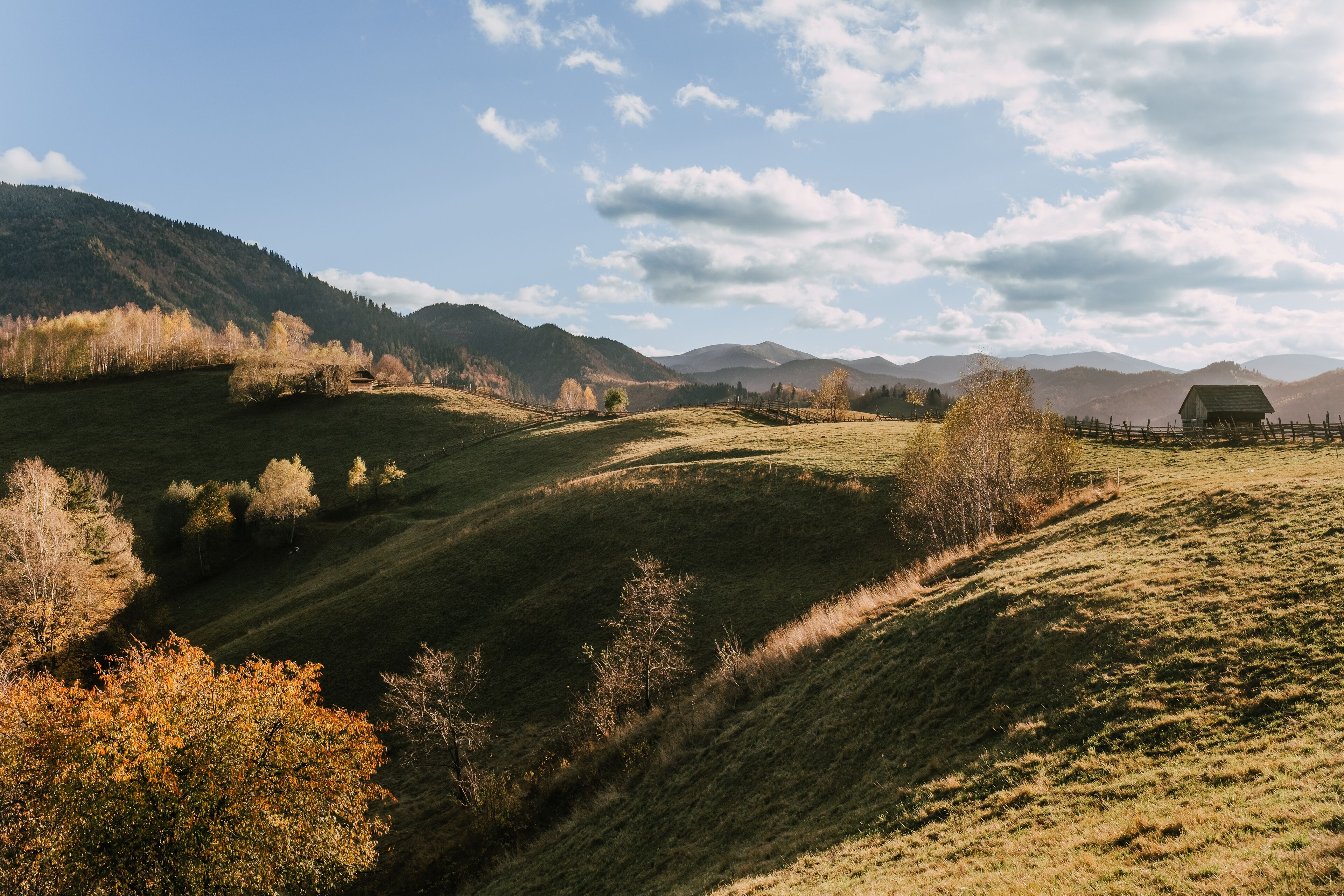 A rural landscape with rolling hills, a small wooden structure, and a clear sky.