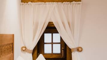 A bedroom with a wooden headboard, a window with white curtains, and a hanging light fixture.
