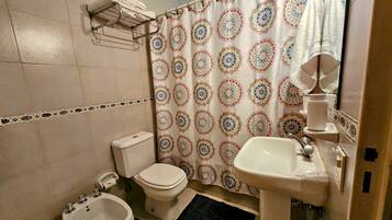 Un baño con inodoro, bidé, lavamanos y una cortina de ducha con un diseño circular.