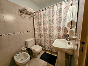 A bathroom with a toilet, bidet, sink, and a shower curtain with a circular pattern.