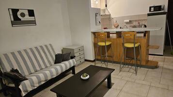 Una sala de estar con sofá, una mesita de centro y una cocina con microondas y taburetes de bar.
