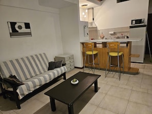 A living room with a sofa, a coffee table, and a kitchen area with a microwave and bar stools.