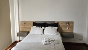 Een slaapkamer met een bed, twee nachtkastjes, een hanglamp en een deur.
