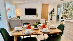 A dining area with a wooden table set for four, surrounded by green chairs. A flat-screen TV is mounted on the wall above the table. - Peaceful & Private Waterfront Retreat w/Heated Pool near Beach & Downtown Stuart (Stuart)
