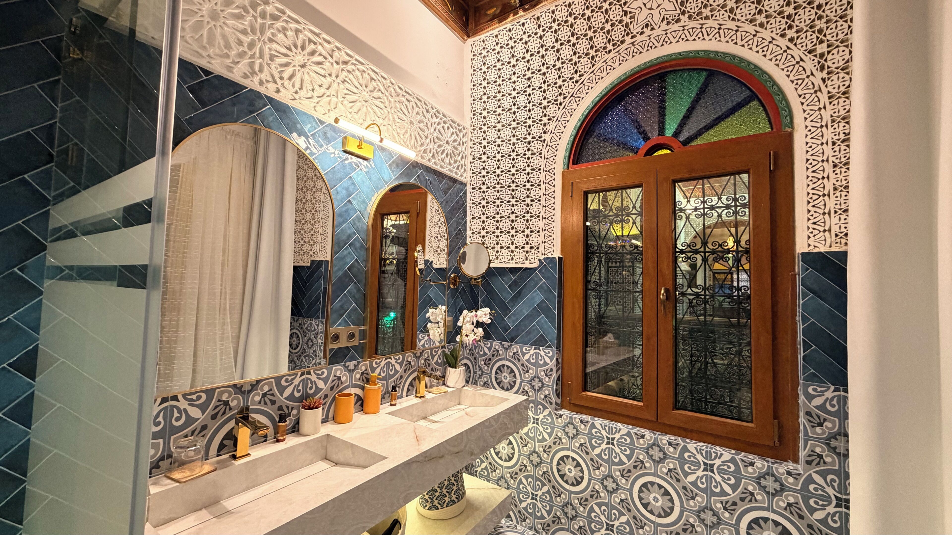 A bathroom with a large mirror, a sink with a vanity, and a window with intricate tile work.