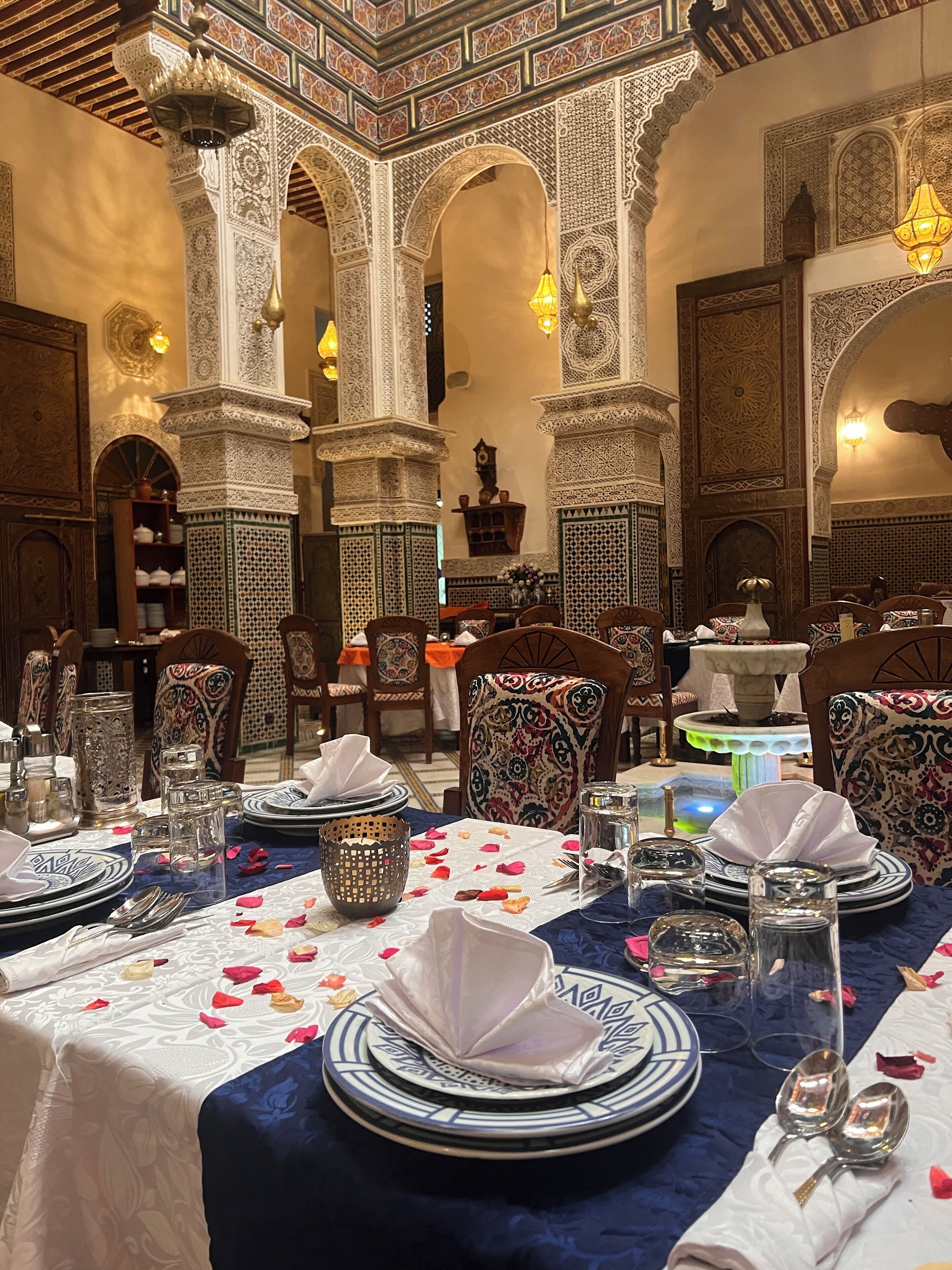 Un espace de restauration marocain traditionnel, agrémenté d’arcs décoratifs, de motifs complexes en mosaïque et d’une variété d’éléments de décoration de table, notamment des assiettes, des verres et des couverts.