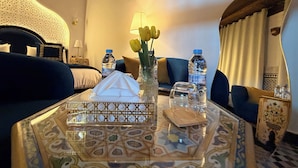 Ett hotellrum med en säng, två soffor, ett soffbord med ett dekorativt bricka, en vas med gula blommor och vattenflaskor.