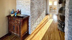 Una habitació espaiosa amb un sostre alt, parets de pedra i terres de fusta. Hi ha un armari de fusta amb figures a la part superior.