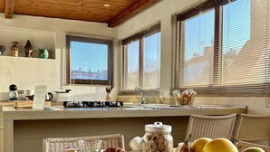 Esmorzar amb un bol de fruita, una tassa i un envasament de cereals damunt d'una taula en una habitació amb bigues de fusta i grans finestres.