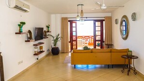 A living room with a yellow sofa, a TV on a shelf, a potted plant, and a ceiling fan.