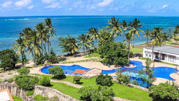A resort with a large pool area, palm trees, and a view of the ocean.