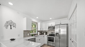 A modern kitchen with white cabinetry, stainless steel appliances, a marble backsplash, and a central island. - Luxury place - 23019 in Port Charlotte , one block to the Bayfront Park/Harbor (Port Charlotte)