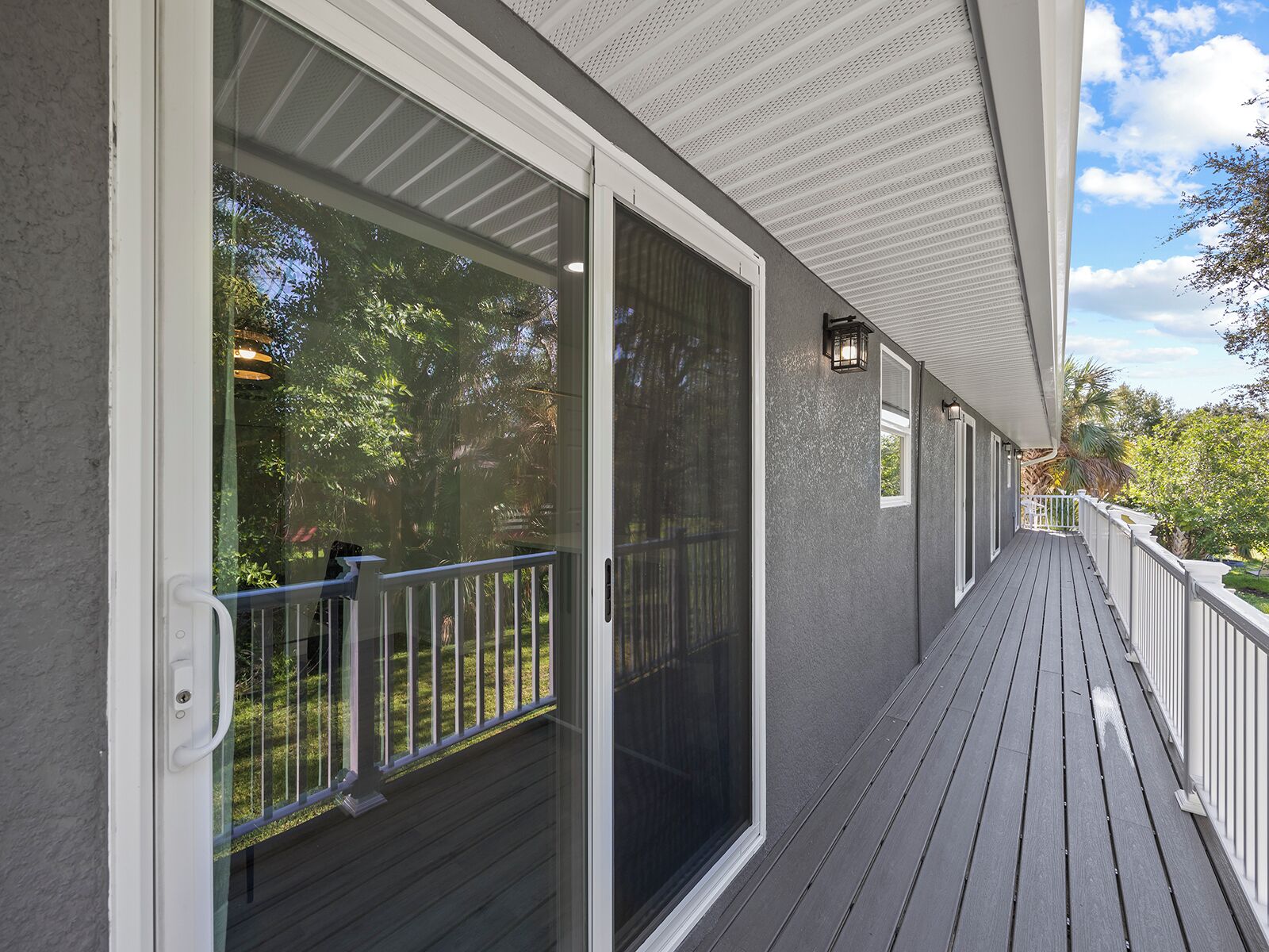 A covered outdoor area with a wooden deck, a glass door, and a white railing.