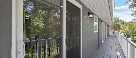 A covered outdoor area with a wooden deck, a glass door, and a white railing.