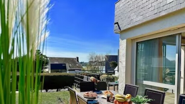 Un espace de restauration en plein air avec une table dressée pour deux personnes, des chaises et un verre de jus d’orange.