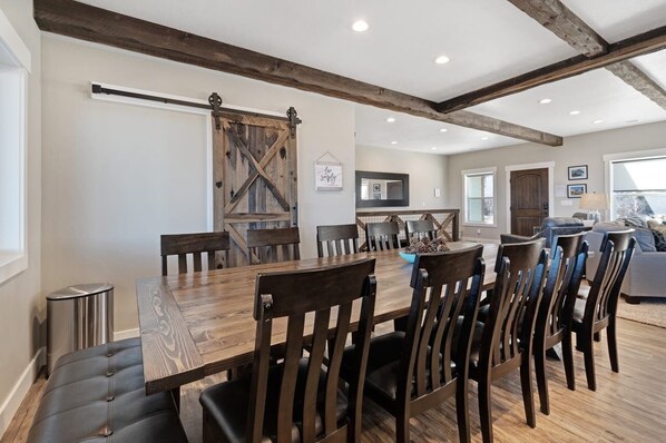 Un coin repas avec une table et des chaises en bois, une porte de grange rustique et, au fond, une cuisine moderne.