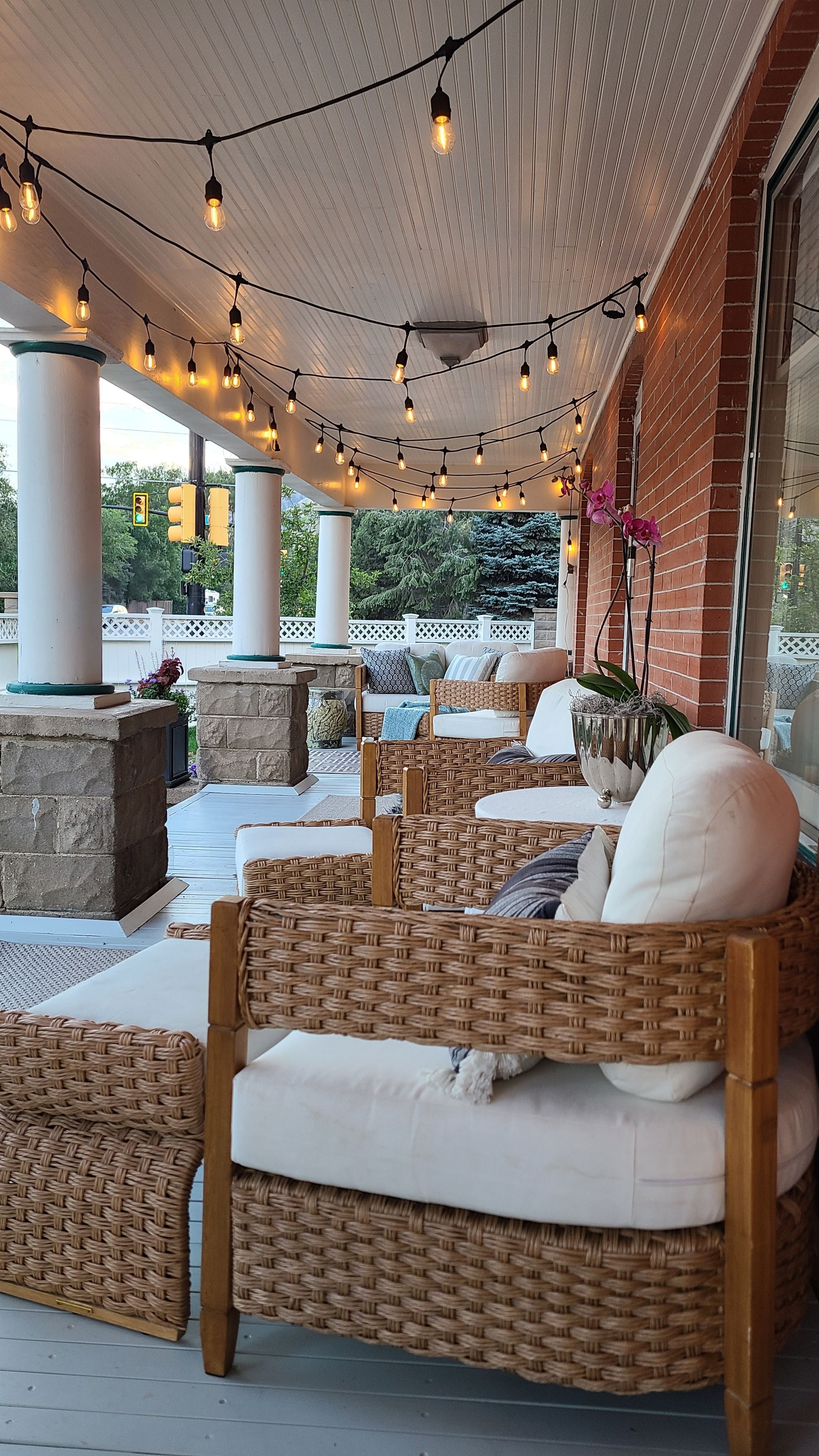 An outdoor seating area with wicker furniture, string lights, and a brick wall.