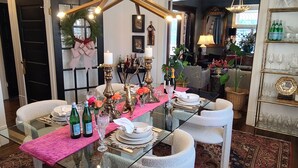 Uma sala de jantar com mesa de vidro posta para seis pessoas, rodeada por cadeiras estofadas brancas.