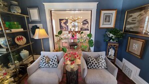 Uma sala de estar com sofá, mesa lateral com um vaso de flores e estante com objetos decorativos.