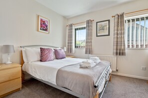 Une chambre à coucher bien rangée, avec un lit, une table de chevet, une lampe et une fenêtre avec des rideaux.