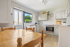 Une cuisine moderne avec des meubles blancs, une table à manger en bois et une vue sur la verdure à l’extérieur.